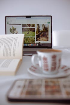 Cozy setup with a laptop, open book, and coffee cup on a white table.